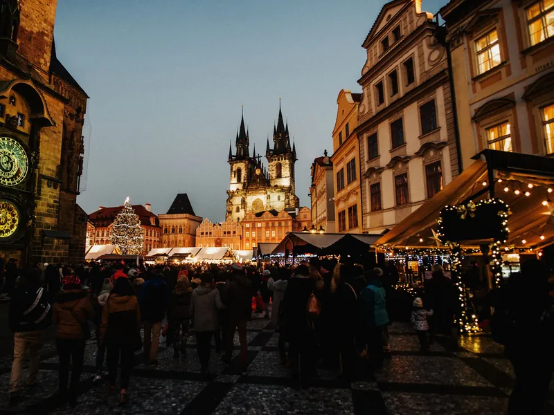 Staroměstské náměstí za modré hodiny: orloj, Týnský chrám a rozsvícený vánoční strom nad stánky